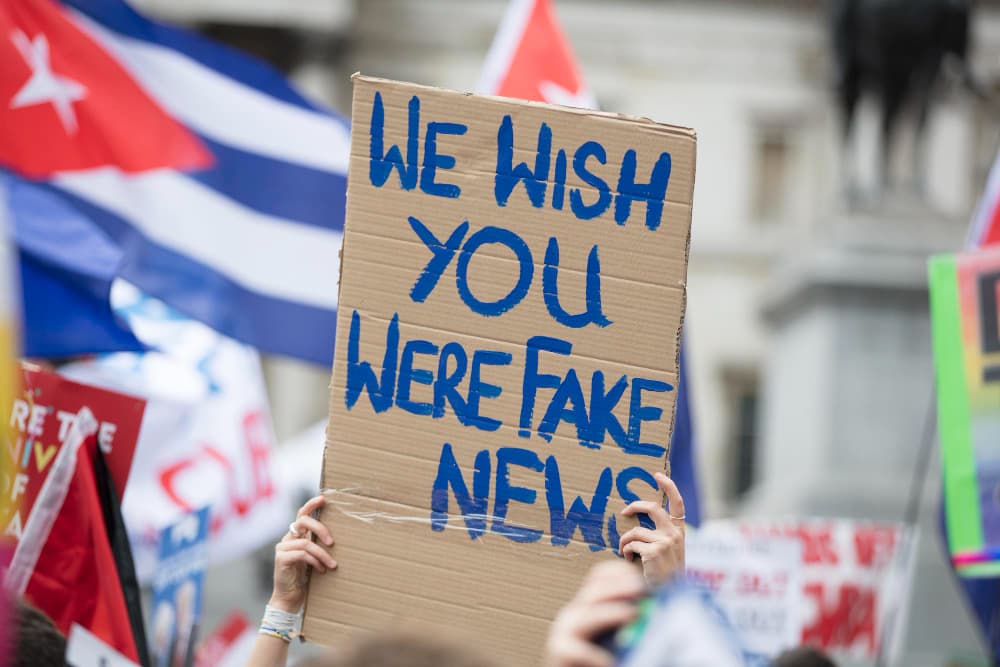 23865454-640px-Opt Protest sign held above the crowd that reads, "We wish you were fake news."